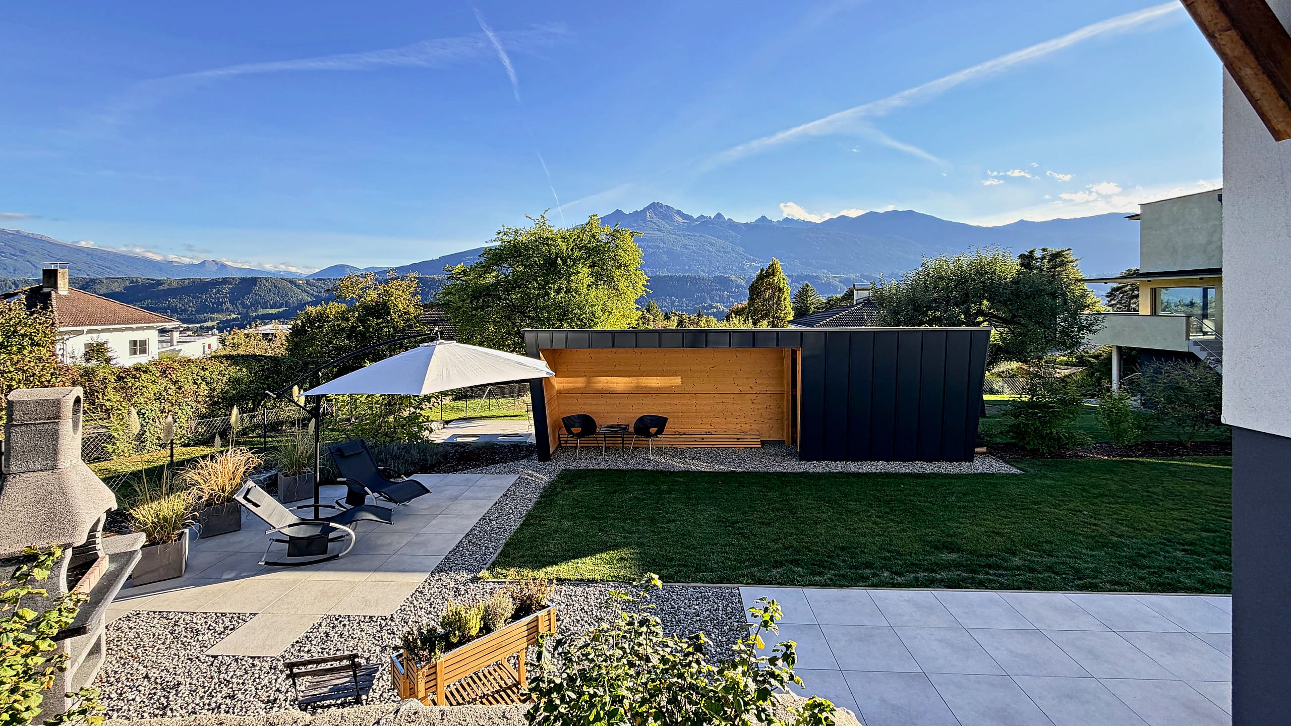 Garden with patio, sun loungers, parasol and a built-in barbecue, with the mountain panorama above the Inn valley behind