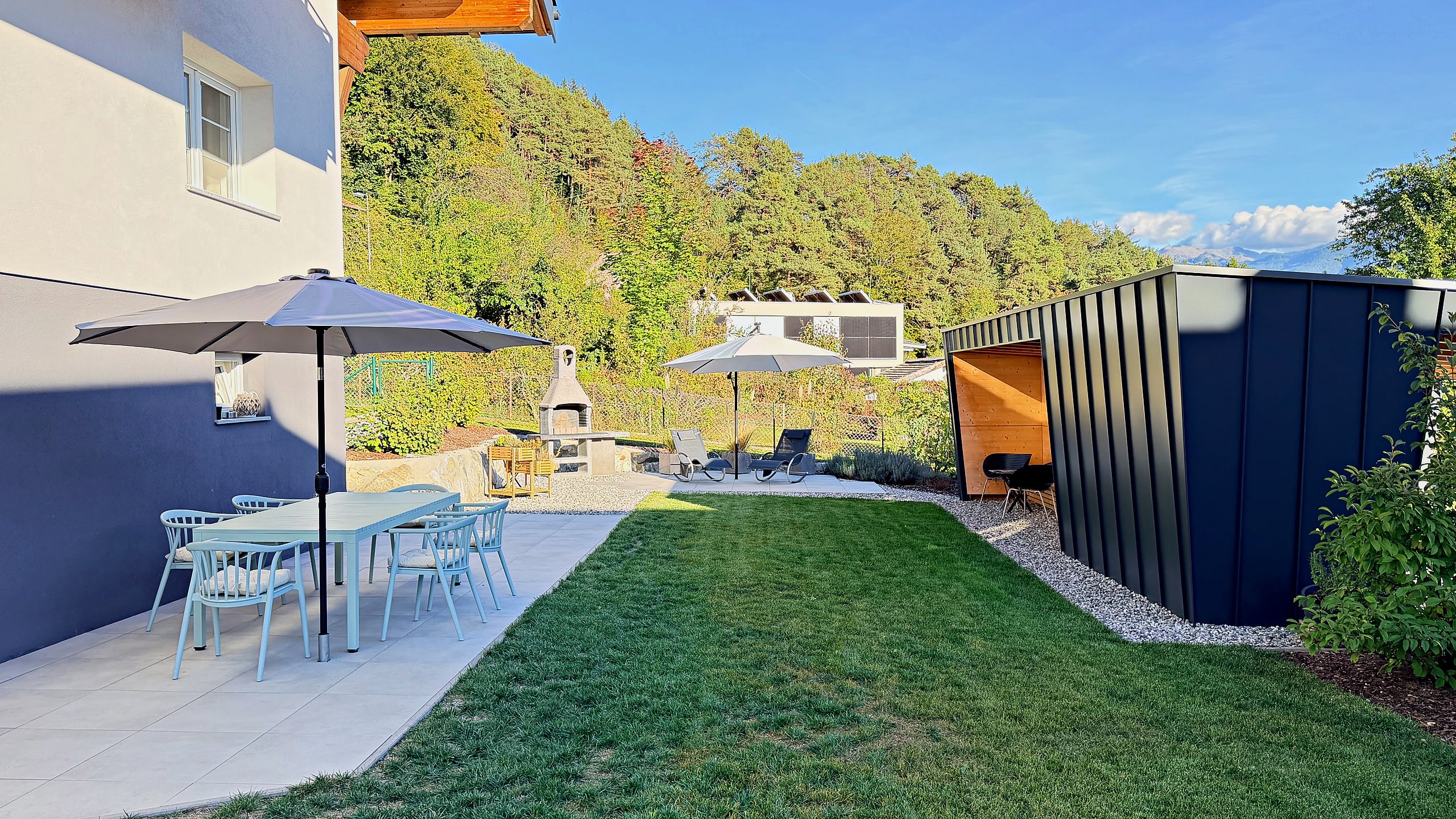 Patio with dining table, chairs and parasol right by the house, next to the garden